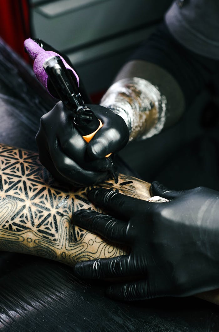 hero-img-01 Tattoo artist working on intricate black and white design indoors.