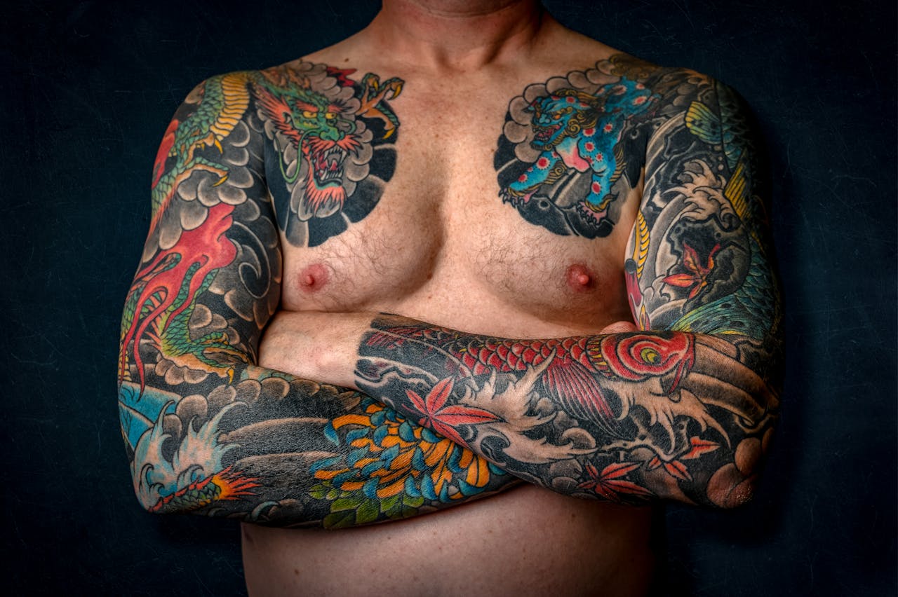 why-choose-us Close-up of a shirtless man with colorful sleeve tattoos and chest art.