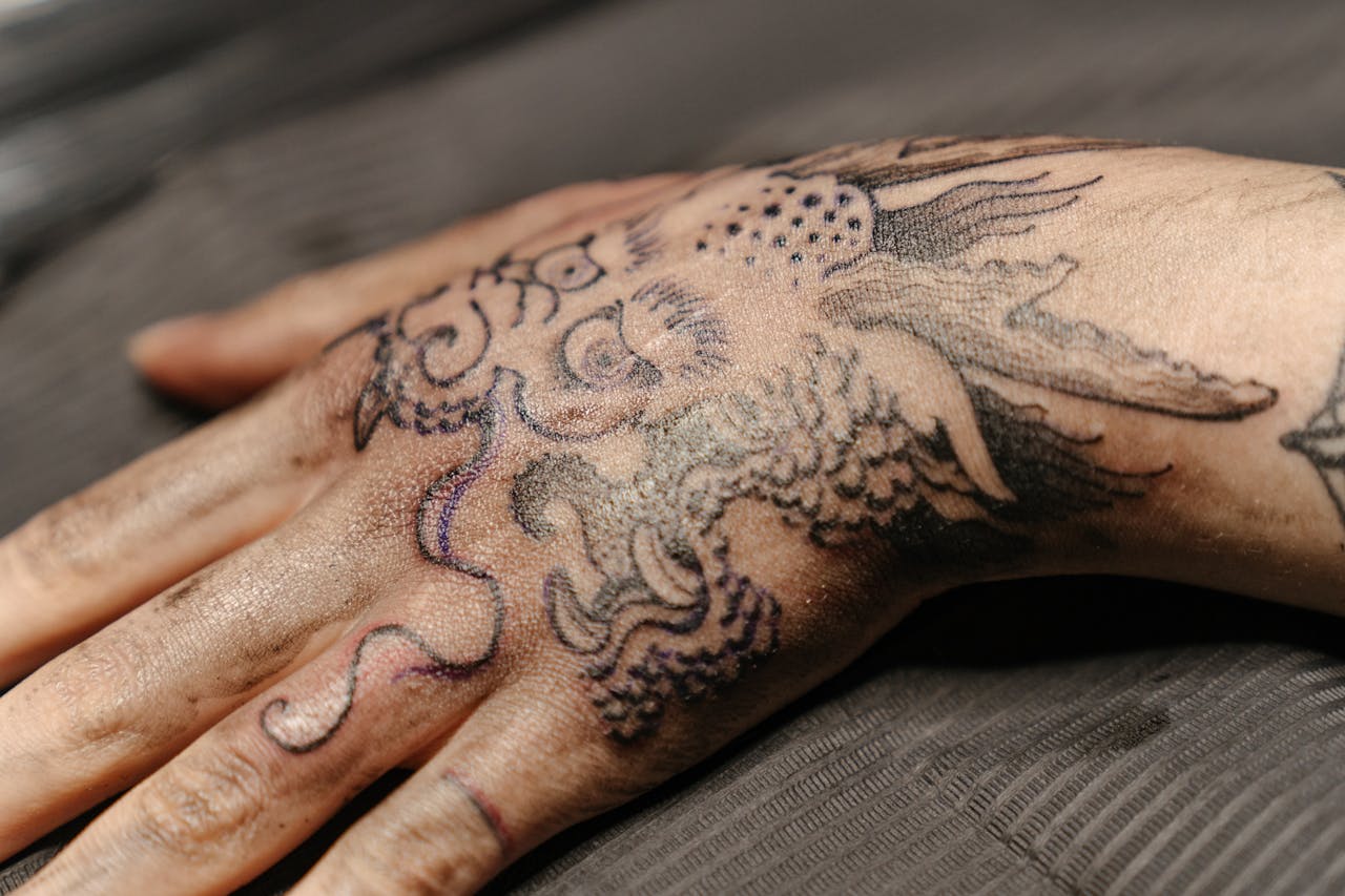 hero-img-02 Close-up view of a detailed hand tattoo featuring a dragon design in a tattoo studio.